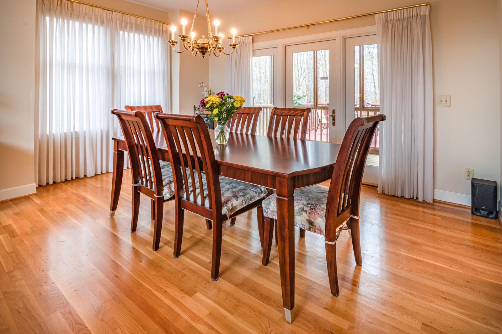 A cherry dining table with six matching chairs on golden oak boards, under a brass chandelier.