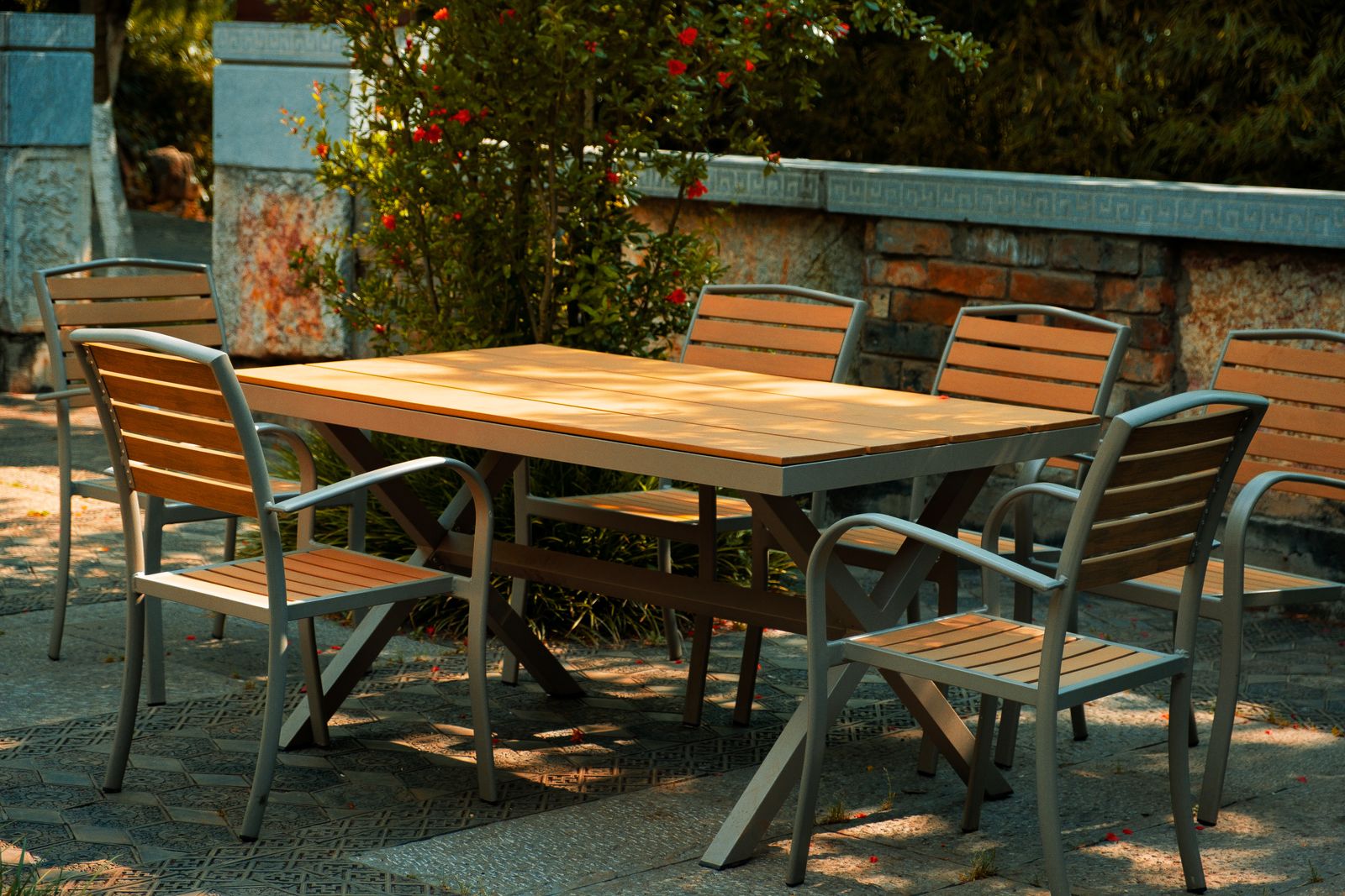 A six-seat patio dining set with a slatted table and matching armchairs, standing in dappled shade.