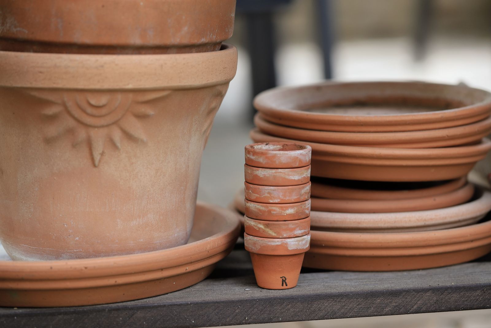 Terracotta pots and saucers stacked on a weathered shelf, one of them embossed with a sunburst.